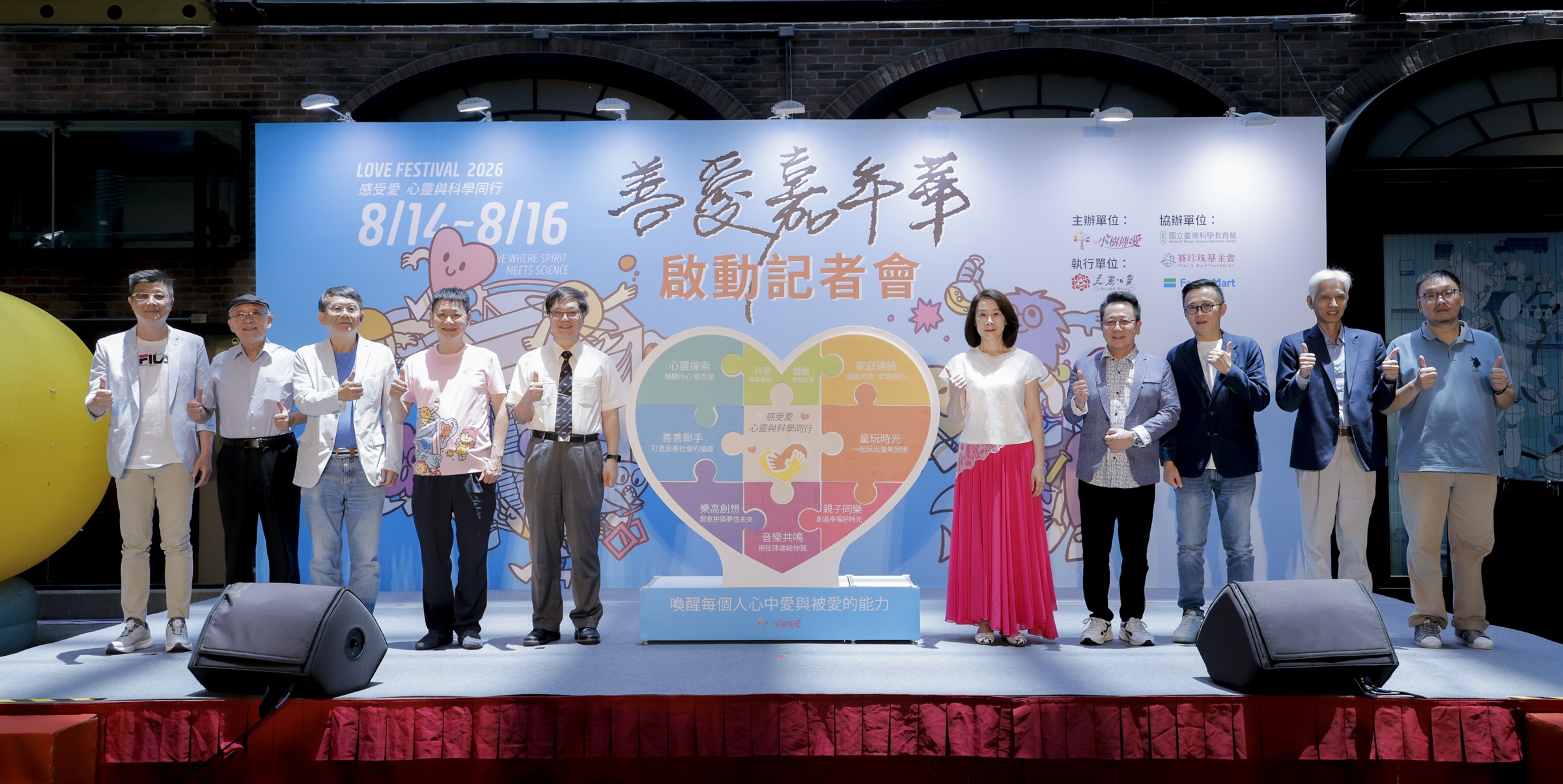 2026 善愛嘉年華啟動記者會,十位與會貴賓於活動主視覺與「八大主題」愛心拼圖前合影